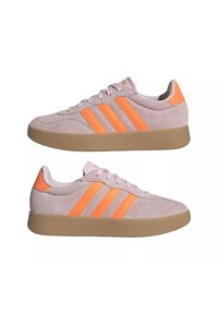 Baskets Adidas en suède violet clair avec des bandes orange et languette à talon, semelle en caoutchouc, vues de profil gauche et droit.