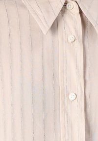 Lys beige skjorte med knappelukking og krage, med vertikale striper og hvite knapper. Stoffet har en jevn tekstur.