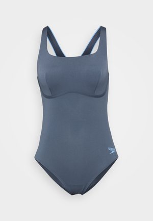 Étthutt i ett stykke i mørkeblå farge med en jevn tekstur, med brede stropper og en subtil merkevarelogo i lyseblå.