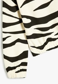 Tissu rayé zèbre noir et crème avec un détail de poignet froncé, présentant une texture lisse et des motifs ondulés audacieux.