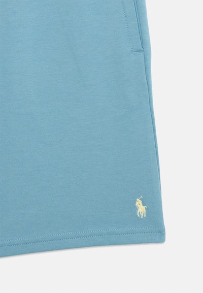 Ανοιχτό μπλε ένδυμα με μικρό κεντημένο κίτρινο λογότυπο αλόγου και αναβάτη κοντά στο κάτω τελείωμα.