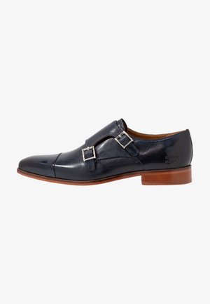 Zapato de vestir de cuero negro con doble tira de monje, hebillas plateadas y suela marrón, tacón bajo y diseño de puntera.