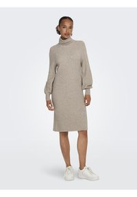 Beige stickad klänning med hög ribbad krage, långa puffärmar och rak skärning. Kombinerad med vita sneakers för en avslappnad stil.