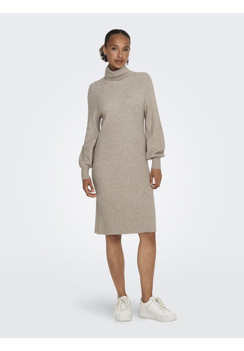Abito in maglia beige con colletto alto a coste, maniche lunghe a sbuffo e taglio dritto. Abbinato a sneakers bianche per un look casual.