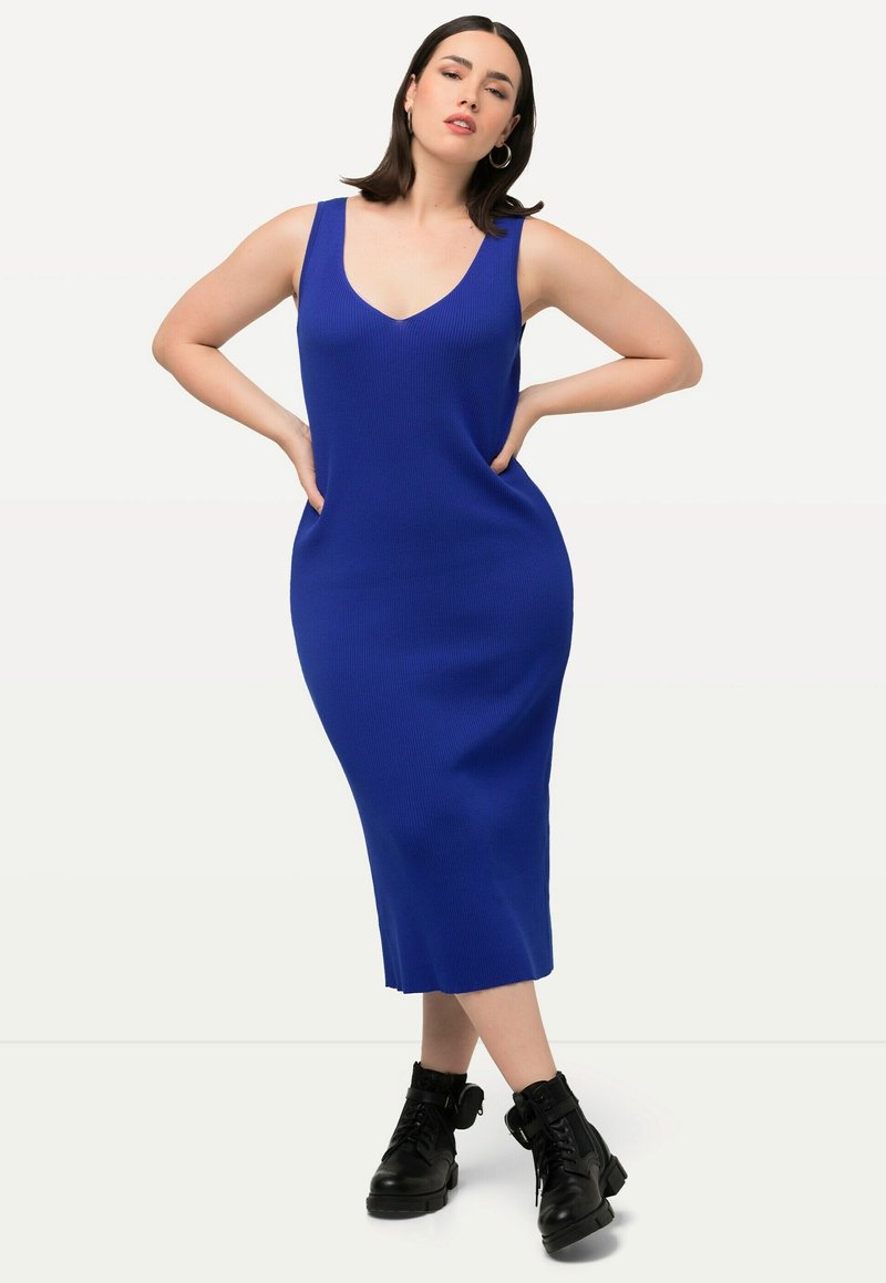 Abito midi blu a coste con scollatura a V e silhouette aderente, caratterizzato da spalline larghe. Indossato con stivali neri chunky con lacci.