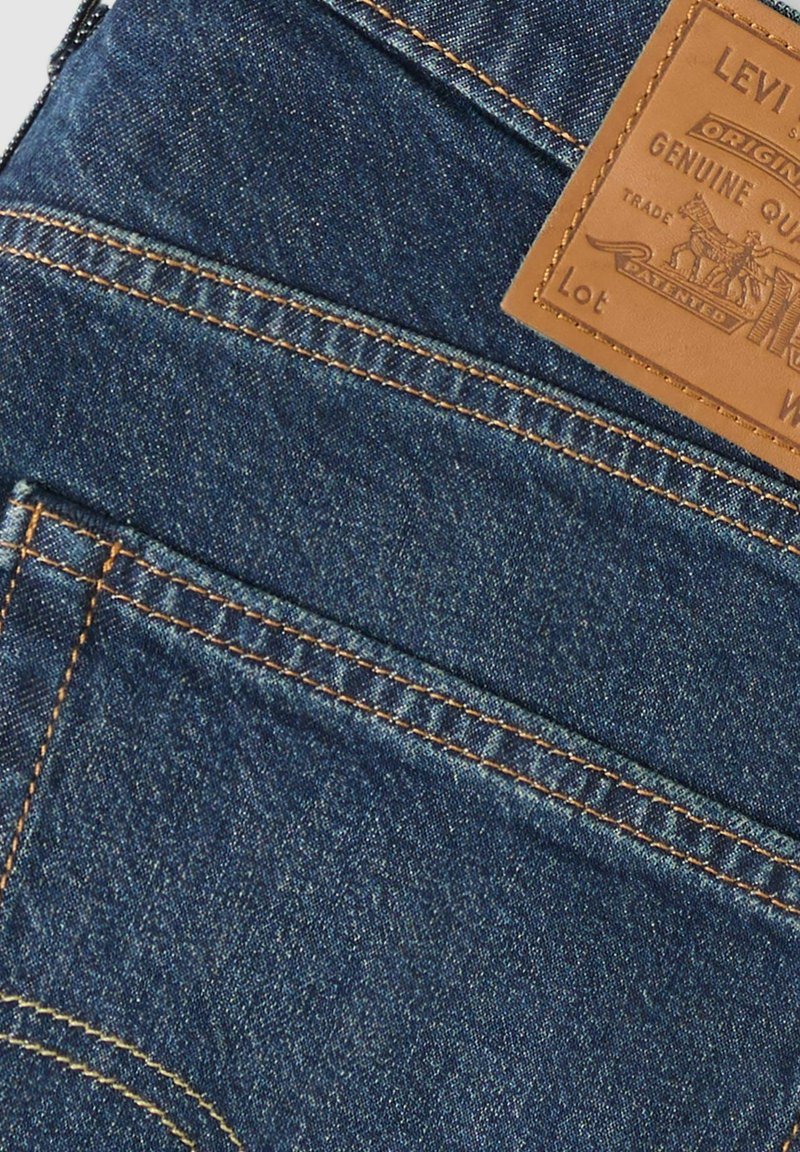 Poche arrière d'un jean en denim avec couture orange et une étiquette de marque Levi's en cuir marron cousue au-dessus de la poche.