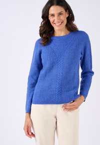 Gebreide blauwe trui met een textuurpatroon, voorzien van een ronde halslijn en lange mouwen, gecombineerd met lichtgekleurde broek.