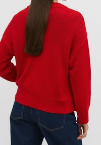 Rode gebreide trui met een losse pasvorm, ribbelzoom en verlaagde schouders. De textuur is chunky met een opvallend steekpatroon.