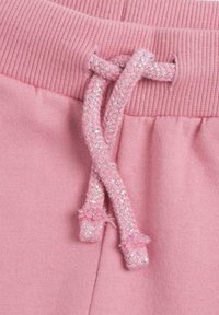 Rosa Jogginghose mit einem breiten elastischen Bund und einer geflochtenen Kordel mit metallischen Fäden, die eine weiche Textur und Pastellfarbe zeigt.