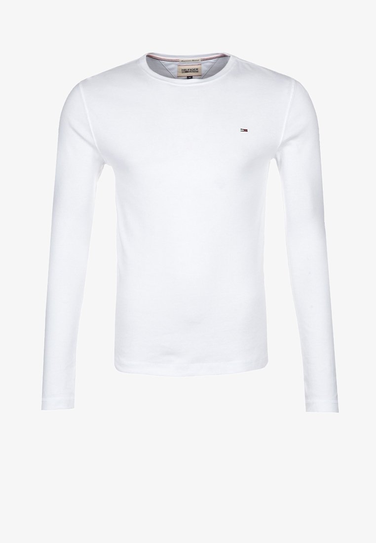 Valkoinen pitkähihainen t-paita, pyöreä kaula-aukko, valmistettu puuvillasta. Pieni brodeerattu logo vasemmassa rinnassa punaisena ja sinisenä. Pehmeä rakenne.
