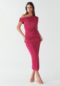 Fuksija haljina s otvorenim ramenima i nabranim detaljima, uskog kroja, rastezljivog materijala, srednje duljine, uparena s bež sandalama na remenčiće.