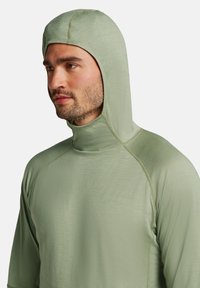 Maglione leggero verde con cappuccio e colletto alto, dalla texture liscia e maniche a raglan, progettato per comfort e protezione.