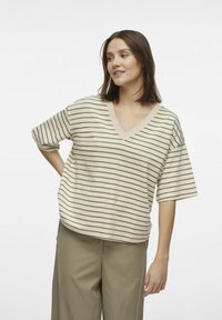 Beżowa bluzka w serek z poziomymi oliwkowymi paskami, z krótkimi rękawami i luźnym krojem, w połączeniu z dopasowanymi khaki spodniami.