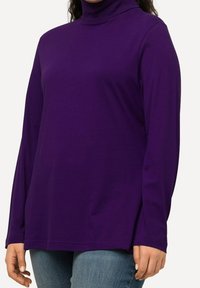 Lila långärmad tröja med polokrage gjord av mjukt tyg, med avslappnad passform och rak fåll, i kombination med denimjeans.