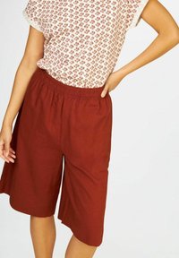 Shorts culottes en lin rouge avec une taille élastique. Présente une coupe décontractée et arrive juste au-dessus du genou. Design simple et unicolore.