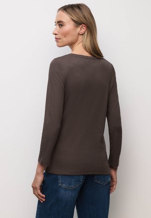 Maglia marrone a maniche lunghe in materiale morbido con scollo rotondo. Il design presenta una vestibilità rilassata ed è abbinato a pantaloni di denim blu.