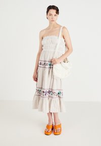 Strapless, witte gestreepte maxi-jurk met geborduurde bloemenpatronen, gerimpelde zoom, gecombineerd met een oranje dikke sandaal en een witte tas.