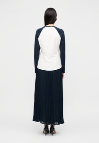 Saia longa azul-marinho plissada combinada com um top branco com mangas raglan azul-marinho. Sapatos pretos de salto completam o conjunto.