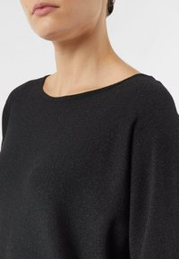 Czarny sweter o miękkiej fakturze i subtelnym blasku. Posiada okrągły dekolt oraz luźny krój, który podkreśla komfort i łatwość noszenia.