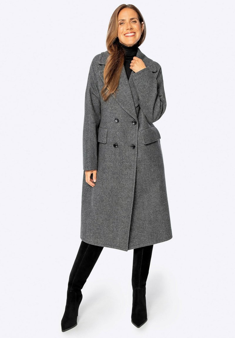 Cappotto grigio in misto lana con chiusura doppiopetto, rever a scendere e due tasche anteriori. Indossato con un dolcevita nero e stivali al ginocchio.