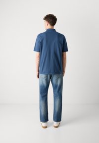 Ναυτικό κοντομάνικο πουκάμισο με γιακά, συνδυασμένο με ανοιχτό μπλε τζιν. Το σύνολο έχει χαλαρή εφαρμογή και ελάχιστες λεπτομέρειες σχεδίασης.