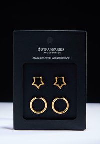 Set di orecchini in acciaio inossidabile dorato, composto da un paio a forma di stella e un paio di orecchini a cerchio rotondi, entrambi confezionati su un cartoncino nero.
