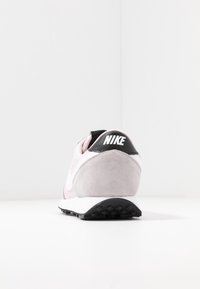 Nike-sneaker med en övre del i rosa och grå mocka, svart hälkappa och vita accenter. Har en strukturerad sula och logotyp på hälen.