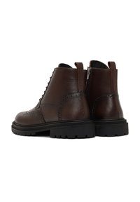 Bottes chelsea en cuir marron avec une finition texturée, présentant des détails brogue, une semelle en caoutchouc noir robuste et une fermeture éclair sur le côté pour un enfilage facile.