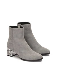 Botas de tobillo de ante gris con punta afilada, cierre de cremallera y un acento de tacón de bloque plateado geométrico. Textura suave y diseño minimalista.