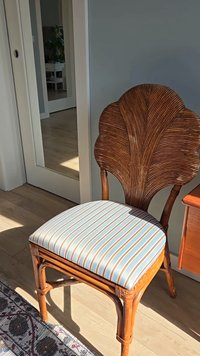 Ratanová stolička s opierkou vo tvaru ventilátora, pruhovaným modro-bielym polstrovaným sedadlom, drevenými nohami a teplým prírodným povrchom.