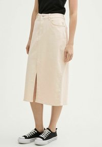 Helle rosa Jeansrock mit Frontschlitz, hoher Taille und fünf Taschen, kombiniert mit schwarzen Sneakers mit weißen Sohlen und Schnürsenkeln.