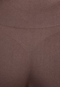 Braune Leggings mit geripptem Muster und nahtlosem Design, die einen konturierten Bund und eine glatte Stoffoptik hervorheben.