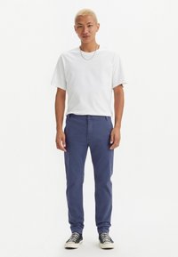 Camiseta branca de gola redonda, calças azul-marinho e ténis preto e branco. Tecido em algodão, corte descontraído, com as bainhas das calças dobradas.