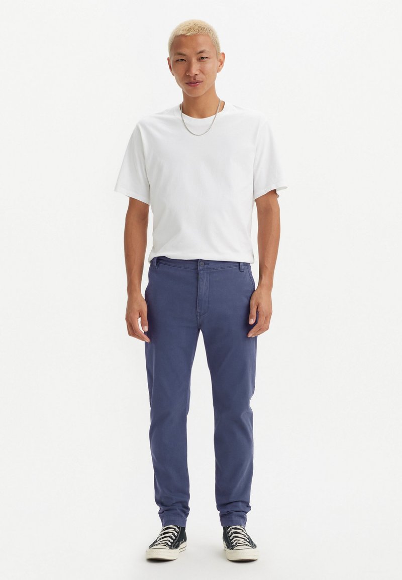 Camiseta blanca de cuello redondo, pantalones azul marino y zapatillas en blanco y negro. Tejido de algodón, corte relajado, con los puños de los pantalones doblados.