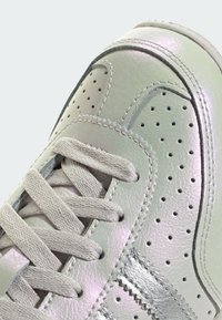 Gaiši pelēka ādas sporta apava ar perforētām detaļām, sudraba akcentiem un plakanu auklu, ar gludu, spīdīgu tekstūru.