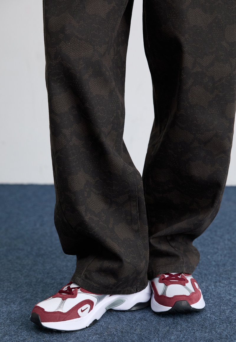 Pantalones negros con estampado hechos de tela texturizada, combinados con zapatillas deportivas de malla blancas y burdeos con suela negra.