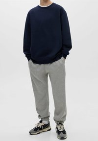 Felpa blu navy con maniche lunghe e collo rotondo, abbinata a pantaloni della tuta grigio chiaro che si stringono alle caviglie. Indossata con scarpe da ginnastica nere e grigie.