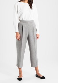 Gray pleated trousers with a high waist, made of textured fabric, paired with a white long-sleeve top. Black pointed flats complete the look.