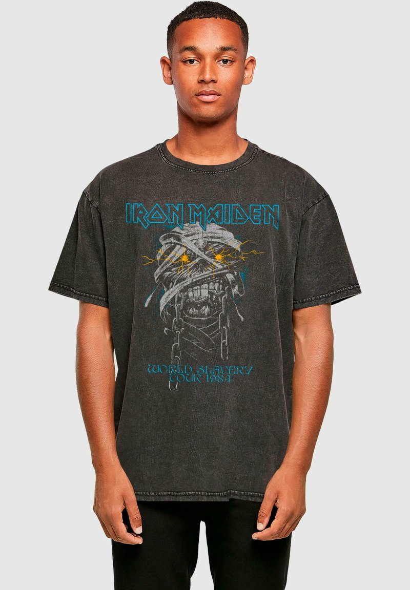 Graues, übergroßes T-Shirt mit einer verblassten Textur, das ein Totenschädel-Motiv und blauen "Iron Maiden"-Text zeigt. Die Vorderseite enthält das Detail "World Slavery Tour 1984".