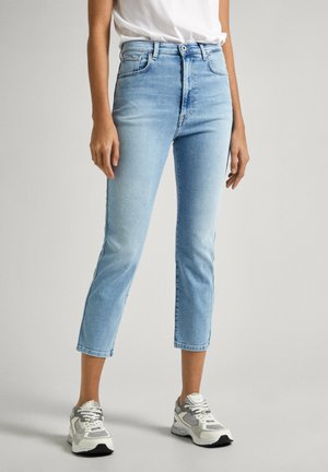 Jeans de mezclilla cortos de color azul claro con una cintura alta, diseño de cinco bolsillos y pierna recta. Llevados con zapatillas gris y blancas.
