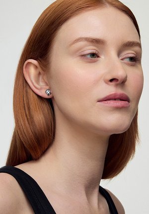 Srebrne kolczyki w kształcie pandy z czarną i białą emalią. Prosty, okrągły kształt z błyszczącym wykończeniem, umiejscowione na uchu modelki.