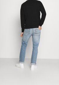 Svart sweatshirt med rund hals, kombinerad med ljusblå smala jeans och vita sneakers. Synliga uppvikta ärmar och detaljer på bakfickan.
