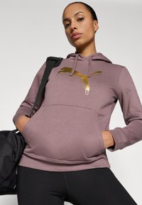 Mauve krāsas pūdera kapuce ar zeltītu Puma logo. Izgatavots no mīkstas auduma, ar kengūra kabatu un ribotām piedurknēm. Melna soma malā.