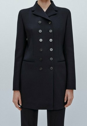 Double-breasted black blazer with peak lapels, ten buttons, and welt pockets, worn with matching black trousers.