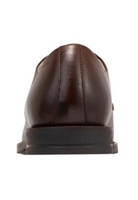 Scarpa in pelle marrone con finitura liscia, forma rotonda e cuciture visibili. Presenta una suola nera bassa e piatta.