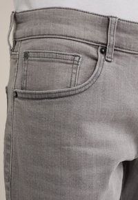 Des jeans en denim gris présentent un design classique à cinq poches et une fermeture à bouton, avec une texture lisse et des détails de coutures subtils.