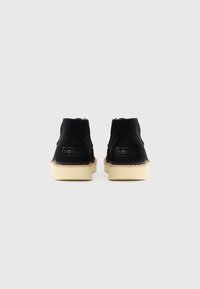 Pair of black suede ankle boots with beige soles, positioned heel-side facing forward on a plain light gray background.