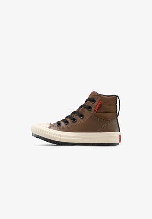 Zapatillas altas marrones con cordones negros, puntera de goma y suela crema en contraste. Cuenta con una parte superior texturizada y una etiqueta de acento roja.