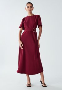 Burgundijas midi kleita ar īsām pūkainām piedurknēm, piesaistīt jostu ar zelta gredzenu akcentu un gludu teksturētu audumu.