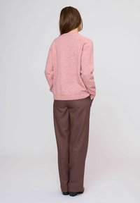 Maglione rosa lavorato a maglia con colletto rotondo, abbinato a pantaloni marrone a scacchi. L'outfit ha una vestibilità comoda e un tessuto strutturato.